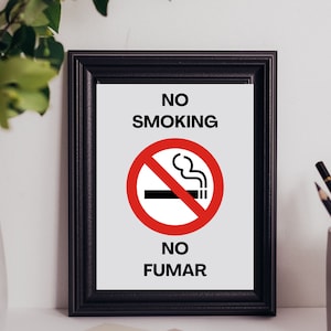 Könnte beinhalten: Ein schwarzer gerahmter Schild mit weißem Hintergrund und dem Text "NO SMOKING NO FUMAR" in Schwarz. Ein roter Kreis mit einem diagonalen Strich enthält ein Schwarzweißbild einer Zigarette mit Rauch.