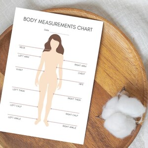 May include: A white Body Measurements Chart with a female figure outline, labeled with body part measurement points. The chart includes the text "BODY MEASUREMENTS CHART" and "Date:" at the top. The chart is on a wooden plate.