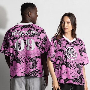 Puede incluir: Camiseta gráfica rosa y negra con ribete blanco. La camiseta presenta el texto "ALLEYCUT" y el número "09" en la espalda. La parte delantera de la camiseta tiene un logotipo circular con las letras "FC". El diseño incluye elementos florales y abstractos.