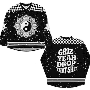 Könnte beinhalten: Schwarzes Langarm-Trikot mit Yin-Yang-Design und Sternen. Das Trikot hat ein Schachbrettmuster auf den Schultern und den Text "Griz Yeah Drop That Shit" auf dem Rücken. Ein einzigartiges und stilvolles Kleidungsstück.