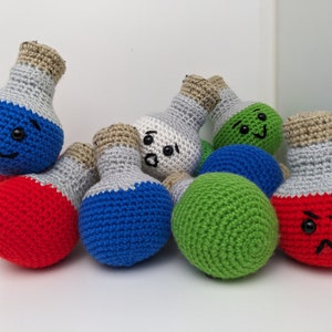 May include: A group of eight crocheted potion bottles with different colored faces. The bottles are in various colors, including red, blue, green, and white.