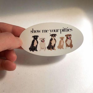 May include: White oval sticker with the text "show me your pitties" in black lettering. Five cartoon pit bull terriers are depicted in a row, each with a different color and pattern.