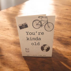 May include: A card with a vintage bicycle, camera, record, and glass of whiskey. The card reads "You're kinda old but I still like you."
