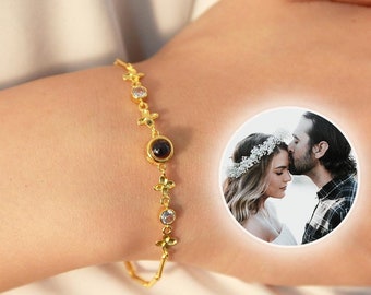May include: A gold bracelet with a small black stone and clear crystals. The bracelet has a small round locket that opens to reveal a photo of a couple.
