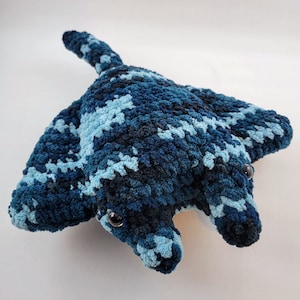May include: A blue and light blue crocheted stuffed manta ray with black eyes.