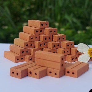 Könnte beinhalten: Ein Stapel Miniatur-Ziegel aus rotem Ton, einige in Pyramidenform gestapelt, andere in einer Reihe angeordnet. Die Ziegel haben jeweils zwei Löcher und sind perfekt für Miniatur-Bauprojekte.