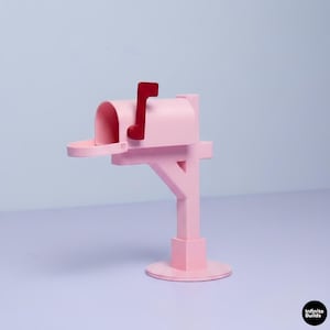 May include: A light pink mailbox featuring a dark red flag on the side, mounted on a matching pink post with a circular base. The mailbox has an open front and is positioned against a light blue background. The text Infinite Builds is visible.
