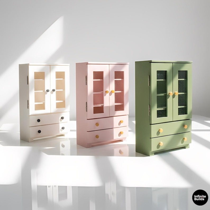 May include: Three miniature wooden cabinets in white, pink, and green. Each cabinet has glass-paned doors, interior shelves, and drawers with round knobs. The cabinets are arranged against a white background.