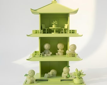 Puede incluir: Una escultura de pagoda verde lima de tres niveles con figuras y muebles en miniatura. La pagoda presenta un tejado, balcones y espacios interiores. Las figuras están en varias poses, algunas sosteniendo hojas o regando plantas. Una pequeña planta está en una maceta.