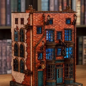 Pode incluir: Modelo de madeira detalhado de um edif&iacute;cio com fachada de tijolo, janelas iluminadas a azul e porta azul-turquesa. O modelo apresenta detalhes arquitet&oacute;nicos intrincados, incluindo candeeiros de rua e um letreiro.