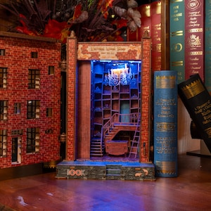 Pode incluir: Diorama de madeira detalhado de uma loja com fachada de tijolo e prateleiras internas, iluminado com luz azul. O diorama &eacute; ladeado por dois livros grandes, um azul e um preto, e colocado contra um fundo de outros livros.