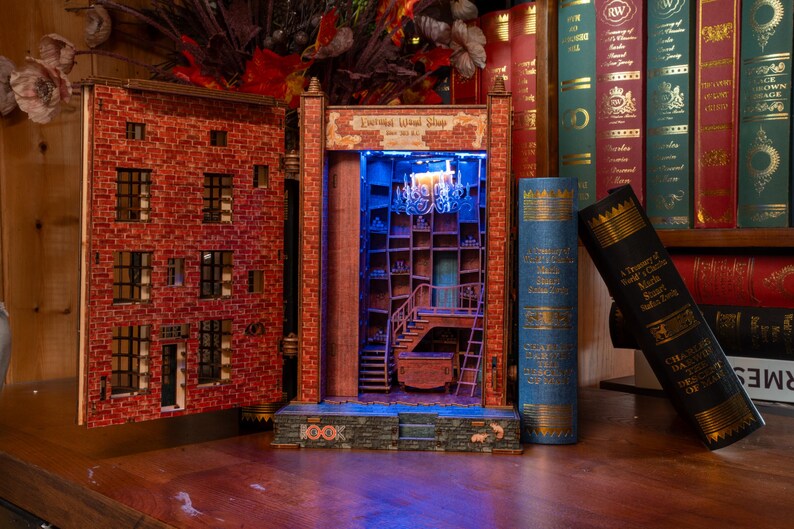 Pode incluir: Diorama de madeira detalhado de uma loja com fachada de tijolo e prateleiras internas, iluminado com luz azul. O diorama &eacute; ladeado por dois livros grandes, um azul e um preto, e colocado contra um fundo de outros livros.