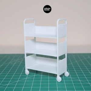 May include: A white three-tiered rolling cart with wheels. The cart is made of plastic and has a simple design.