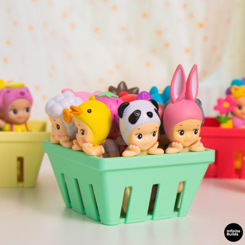 Puede incluir: Una colecci&oacute;n de peque&ntilde;as y coloridas figuras en una cesta verde. Las figuras est&aacute;n vestidas con varios disfraces de animales y alimentos, incluyendo un panda, un pato y un conejo. Otras cestas con figuras similares est&aacute;n en el fondo.