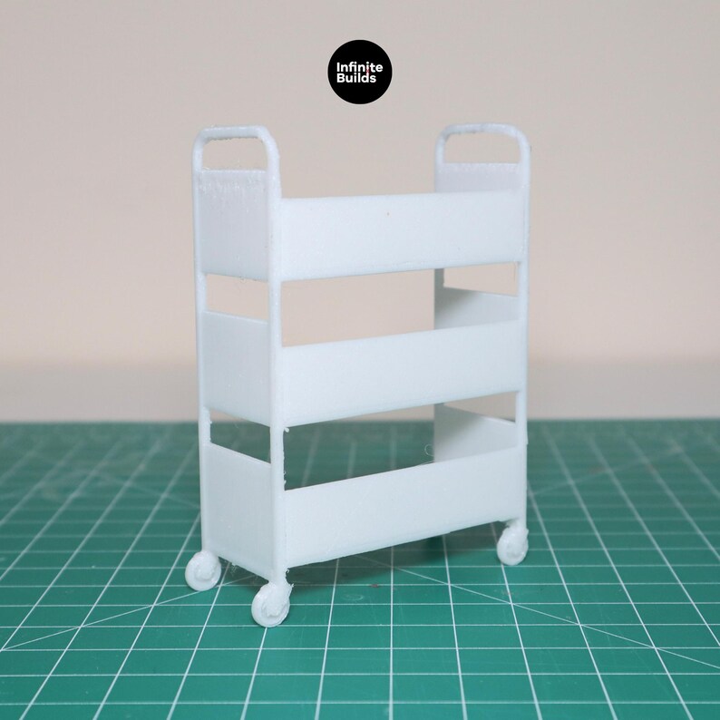 May include: White metal rolling cart with three shelves. The cart has four wheels and is on a green grid surface.