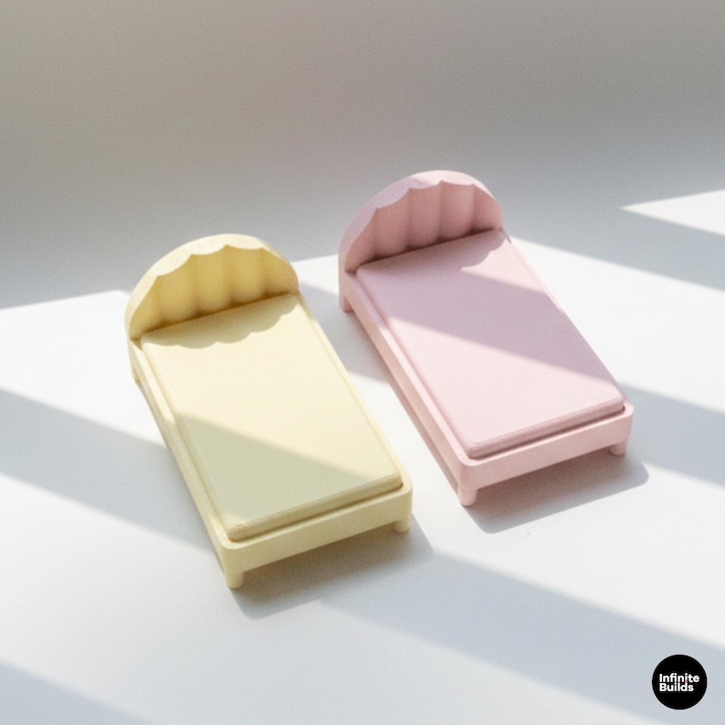 K&ouml;nnte beinhalten: Zwei Miniaturbetten, eines in blassem Gelb und eines in Rosa, werden gezeigt. Jedes Bett hat ein wellenf&ouml;rmiges Kopfteil und eine rechteckige Matratze. Die Betten sind klein, wahrscheinlich f&uuml;r Puppen oder Dekorationszwecke. Die Betten sind aus einem festen Material.
