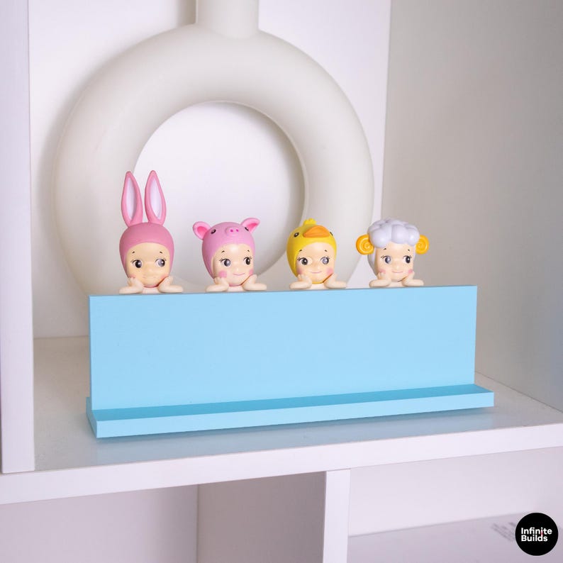 May include: Four small figurines with animal-themed hats, including a bunny, pig, duck, and sheep, are displayed on a light blue shelf. The figurines have a cute, cartoonish design and are set against a white background.