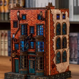 Pode incluir: Modelo de madeira detalhado de um edif&iacute;cio com fachada de tijolo, janelas azuladas e l&acirc;mpadas decorativas. O modelo apresenta um rel&oacute;gio e um letreiro acima da entrada. O interior do edif&iacute;cio &eacute; iluminado por luz azul.