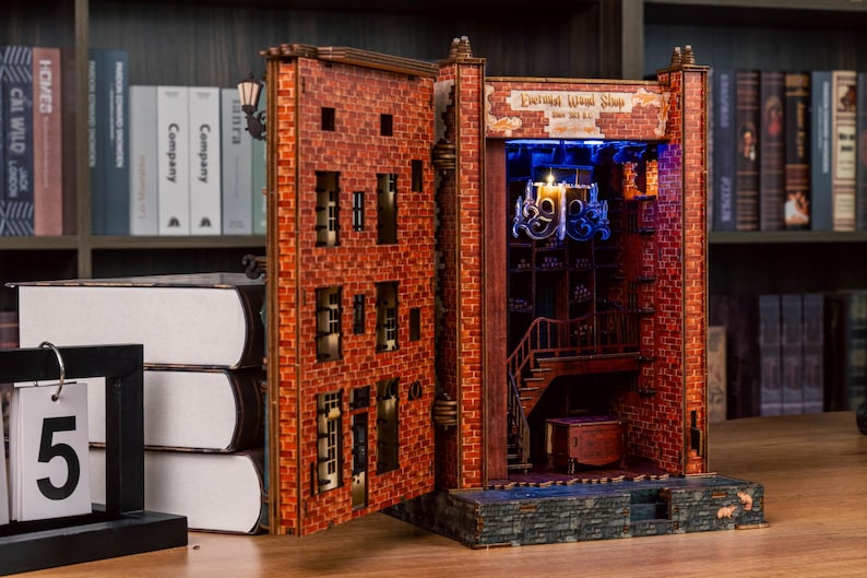 Pode incluir: Diorama detalhado de livro aberto com fachada de tijolos, apresentando um interior de loja com escada e candelabro. O diorama &eacute; iluminado com luzes azuis e amarelas, com o texto "Enchanted Wood Shop".