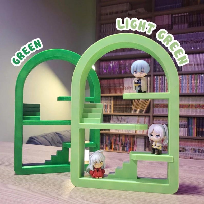 May include: Two green arch-shaped display stands with miniature figurines. One stand is a darker green, labeled "GREEN", and the other is light green, labeled "LIGHT GREEN". The figurines are anime-style characters. The background features a bookshelf filled with books.