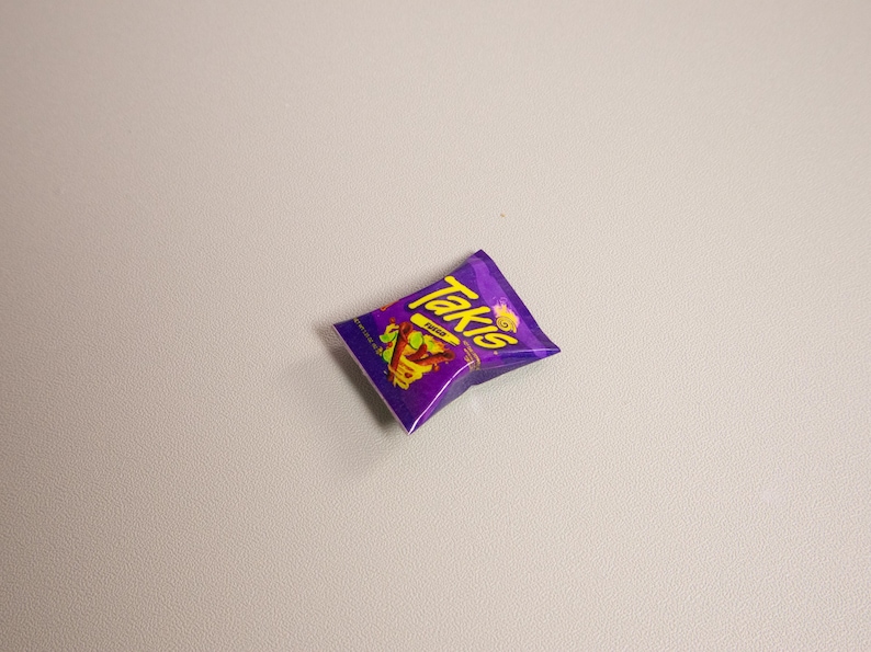 May include: A single, unopened bag of Takis Fuego tortilla chips. The bag is a vibrant purple with yellow and red text and graphics. The chips are a popular snack food.