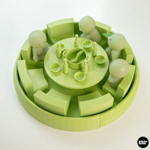 May include: A light green 3D printed miniature dining set featuring a circular table with a central divided pot, four small bowls, and four bottles. Four stylised figures are seated on curved benches around the table. Infinite Builds logo.