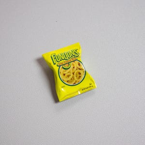 May include: A yellow bag of Funyuns Onion Flavored Rings snacks. The bag has the Funyuns logo in green and yellow, with an image of the onion rings. The bag is on a gray surface.