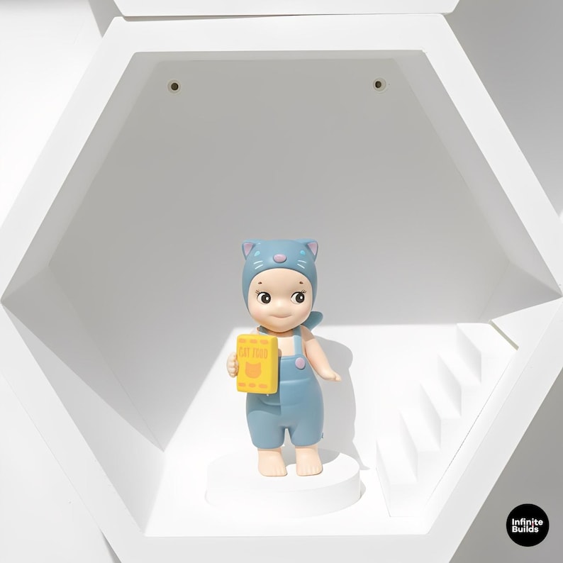 May include: A blue figurine of a child wearing a cat-eared hat and overalls, holding a yellow box of "CAT FOOD". The figurine is standing on a white platform inside a white hexagonal display case.