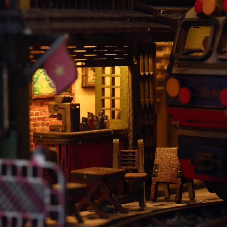 K&ouml;nnte beinhalten: Miniatur-Diorama eines vietnamesischen Caf&eacute;s mit einem Zug im Hintergrund. Das Caf&eacute; hat eine rote Backsteinmauer, eine kleine Bar mit Flaschen und einen kleinen Tisch und St&uuml;hle. Eine Flagge mit einem gelben Stern ist sichtbar.
