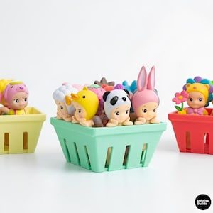 Puede incluir: Una colecci&oacute;n de peque&ntilde;as y coloridas figuras con disfraces de animales y alimentos, como un panda, un pato y una fresa. Las figuras est&aacute;n dispuestas en cestas de pl&aacute;stico de colores pastel, sobre un fondo blanco.