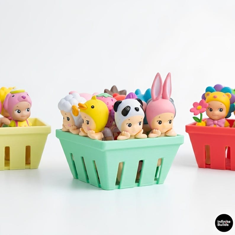 Puede incluir: Una colecci&oacute;n de peque&ntilde;as y coloridas figuras con disfraces de animales y alimentos, como un panda, un pato y una fresa. Las figuras est&aacute;n dispuestas en cestas de pl&aacute;stico de colores pastel, sobre un fondo blanco.