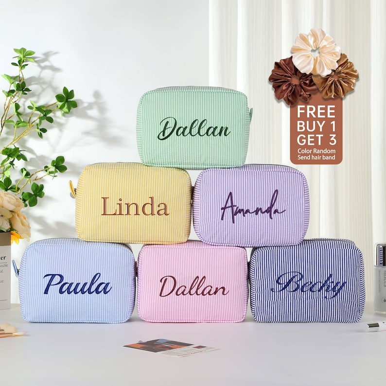 May include: Six striped fabric cosmetic bags with different names embroidered on them. The bags are in various colors, including light blue, yellow, pink, green, purple, and blue. The text "FREE BUY 1 GET 3" is visible in the top right corner of the image.