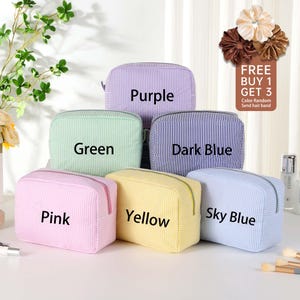 May include: Six striped zippered pouches in different colors: purple, green, dark blue, yellow, sky blue, and pink. The pouches are arranged in a row, with the purple pouch at the top and the pink pouch at the bottom. The text "FREE BUY 1 GET 3" is visible in the top right corner of the image.