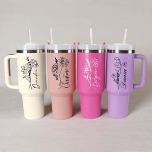 Pode incluir: Quatro canecas t&eacute;rmicas personalizadas em creme, rosa, magenta e lavanda. Cada uma tem um design floral e um nome em escrita cursiva. Possuem tampas brancas, canudos transparentes e al&ccedil;as.