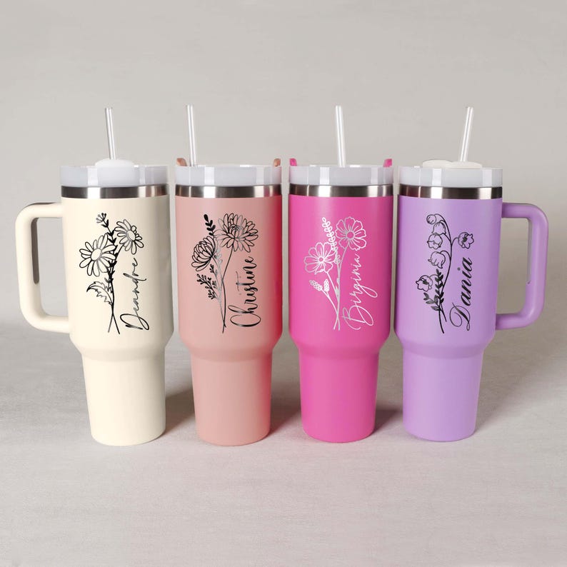 Pode incluir: Quatro canecas t&eacute;rmicas personalizadas em creme, rosa, magenta e lavanda. Cada uma tem um design floral e um nome em escrita cursiva. Possuem tampas brancas, canudos transparentes e al&ccedil;as.