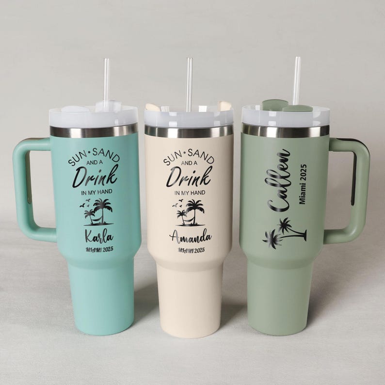 Pode incluir: Tr&ecirc;s canecas isoladas com al&ccedil;as e canudos. As canecas s&atilde;o em tons de verde-azulado, creme e verde s&aacute;lvia. Cada caneca tem uma tampa e apresenta o texto "Sun, Sand, and a Drink in My Hand", um nome e "Miami 2025".