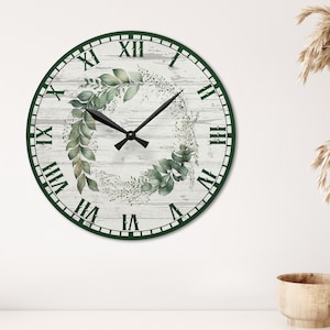 May include: A white and green farmhouse style clock with Roman numeral markings and a leafy wreath design. The clock has black hands and a white background.