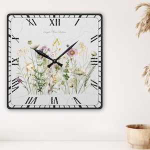 May include: Square wall clock with a black frame and Roman numerals. The clock face features a floral design with wildflowers in shades of purple, yellow, and white. The text "Vintage Flower Selections" is printed on the clock face.