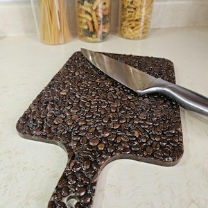 Puede incluir: Una tabla de cortar marrón hecha de granos de café con un cuchillo plateado encima.
