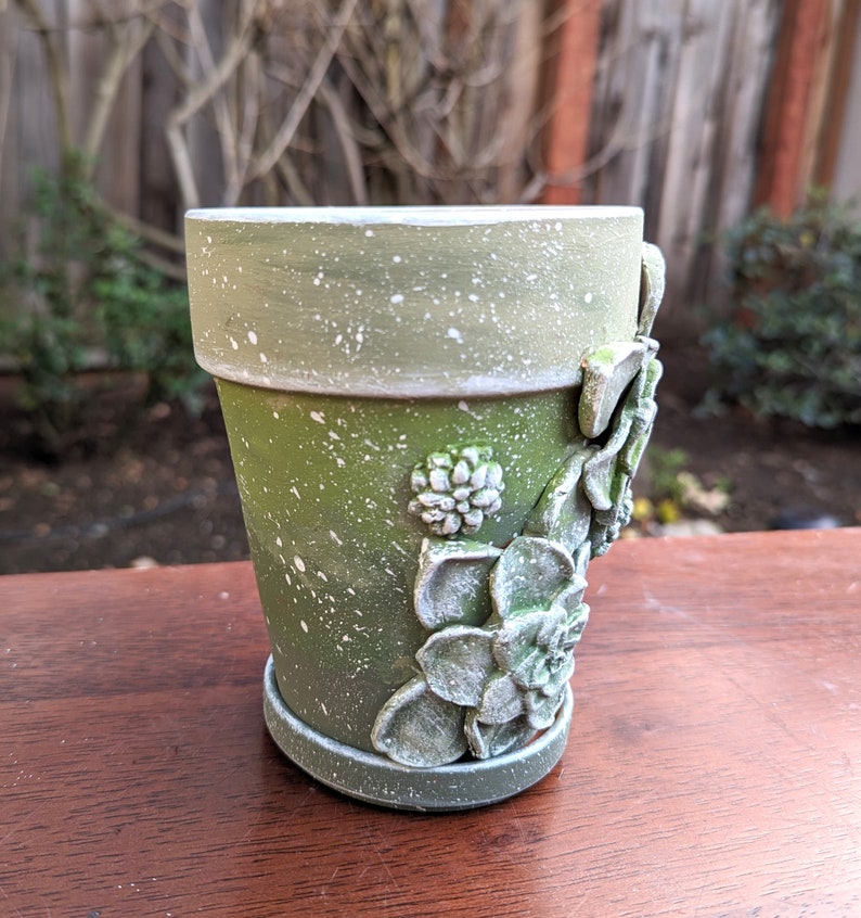 May include: A white ceramic mug with a black handle and the text "But First, Coffee" in a bold, black font. The mug is set against a blurred background, suggesting a cozy setting.