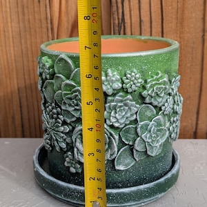 Op de afbeelding: Groene keramische bloempot met reli&euml;f succulent ontwerpen. De pot is ongeveer 18 cm hoog en 15 cm in diameter. Het bevat een bijpassende schotel en heeft een getextureerde afwerking.