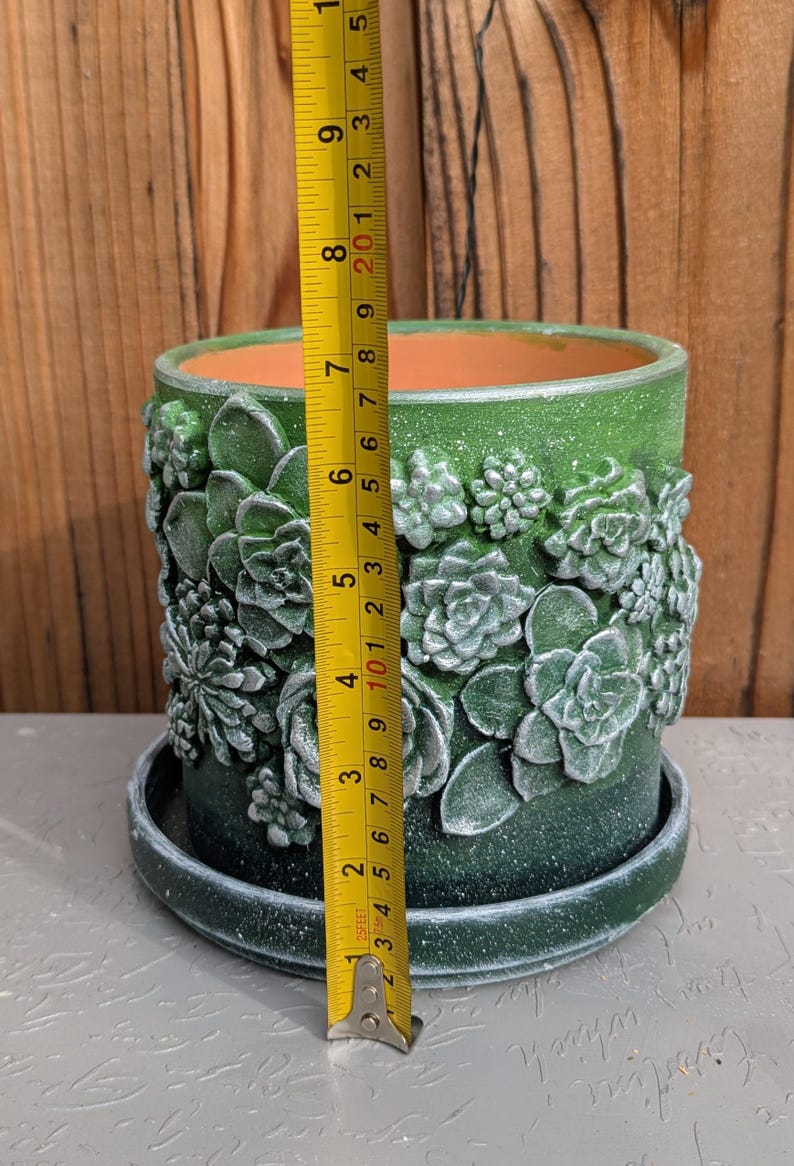 Op de afbeelding: Groene keramische bloempot met reli&euml;f succulent ontwerpen. De pot is ongeveer 18 cm hoog en 15 cm in diameter. Het bevat een bijpassende schotel en heeft een getextureerde afwerking.