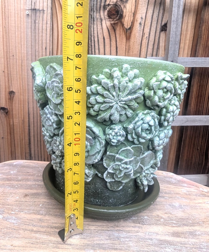 Op de afbeelding: Groene keramische bloempot met een gedetailleerd vetplantenontwerp. De pot is ongeveer 20 cm hoog en heeft een bijpassende schotel. Het getextureerde oppervlak en de reli&euml;fdetails cre&euml;ren een uniek, decoratief stuk.