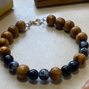 Puede incluir: Un brazalete de madera y piedras preciosas azules con un cierre plateado. El brazalete tiene cuentas de madera y piedras preciosas azules alternadas.