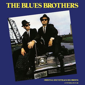 Può includere: La copertina dell'album della colonna sonora del film The Blues Brothers presenta una fotografia in bianco e nero dei due personaggi principali, Jake ed Elwood Blues, in piedi su un'auto. Indossano abiti neri e fedora. L'auto ha una targa dell'Illinois che recita "BDR 529". Il titolo dell'album "The Blues Brothers" è in lettere gialle su sfondo blu.