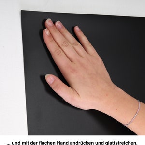 May include: A hand smooths a black surface. The surface is smooth and appears to be made of a material like felt or fabric.