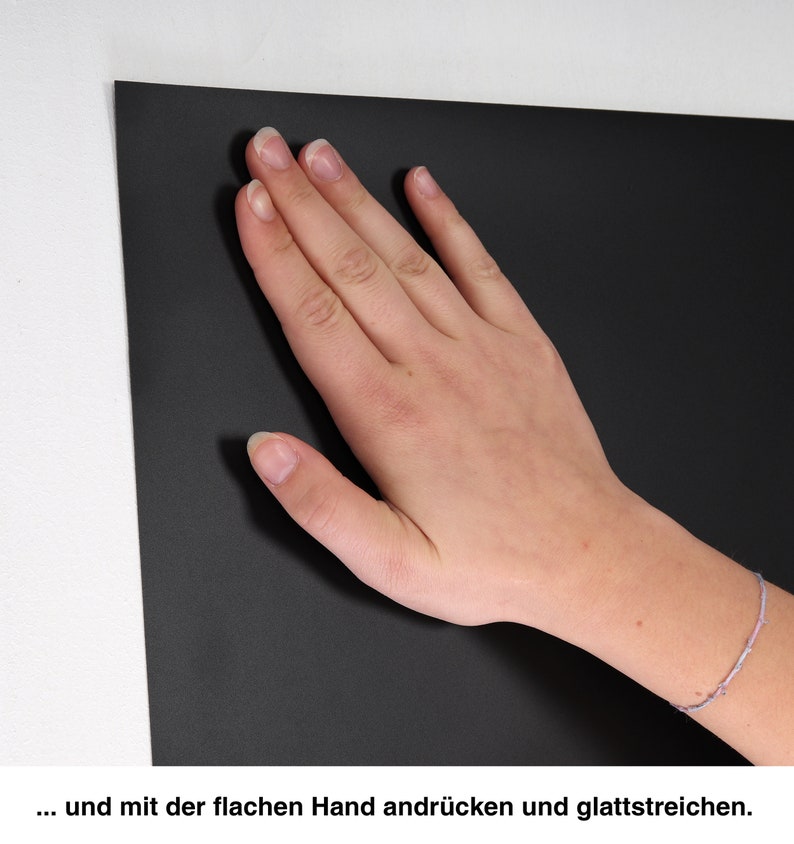 May include: A hand smooths a black surface. The surface is smooth and appears to be made of a material like felt or fabric.