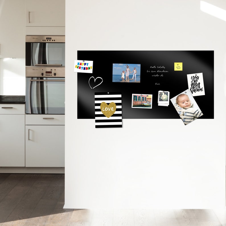 May include: A black magnetic dry erase board with a variety of photos, notes, and decorative items attached to it. The board is mounted on a white wall in a kitchen.