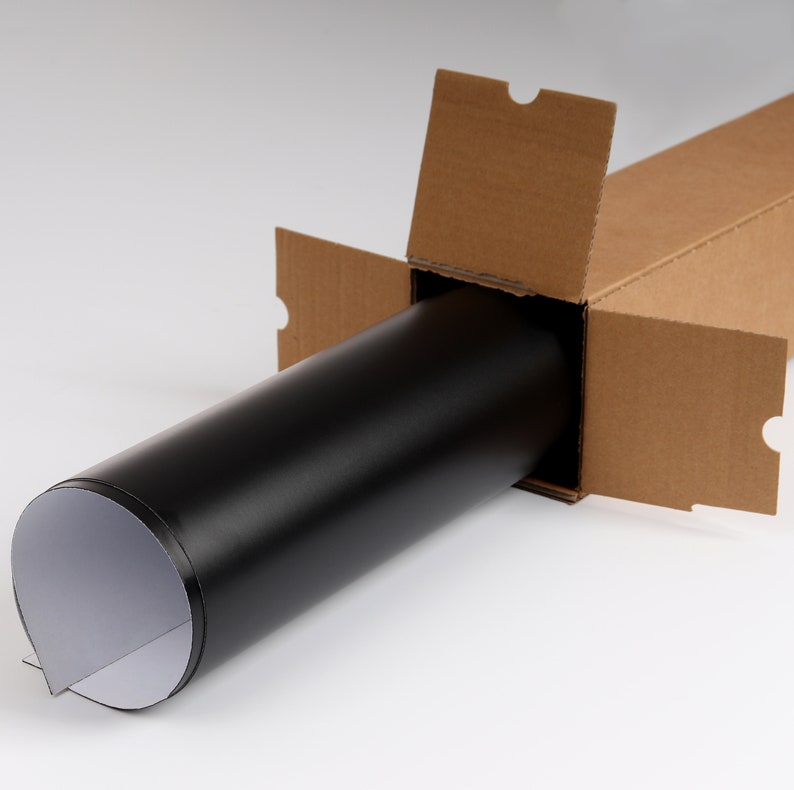 May include: A black roll of material is partially unrolled and placed inside a brown cardboard box. The box is open and the roll is visible.