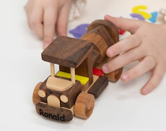 May include: A wooden toy truck with a cement mixer, painted in brown, yellow, and red. The truck has a name, "Ronald", engraved on the front.